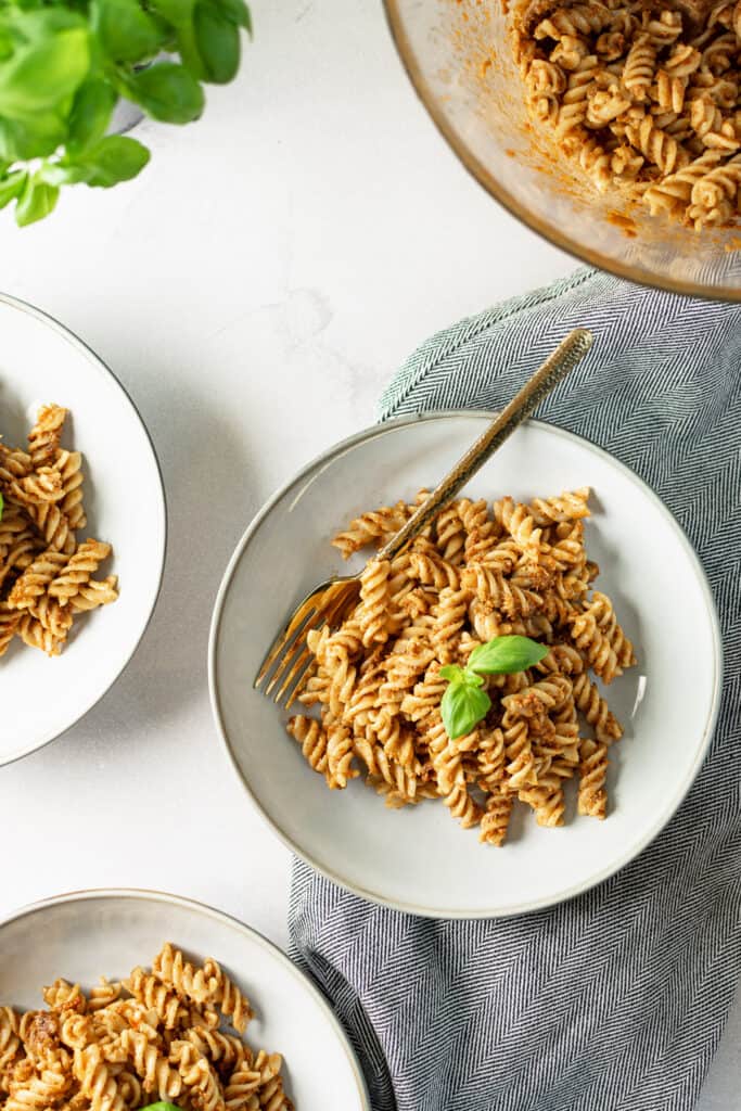 A bowl of red pesto fusilli pasta, topped with basil leaves.